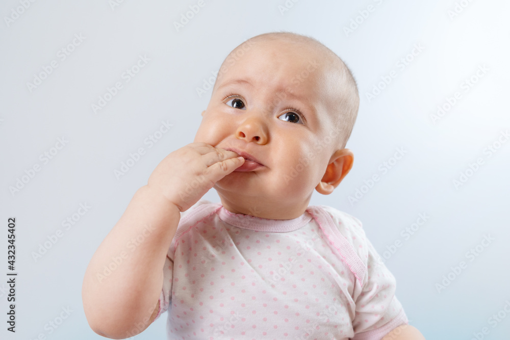 Portrait of sad newborn baby 8-10 months old with hand in mouth
