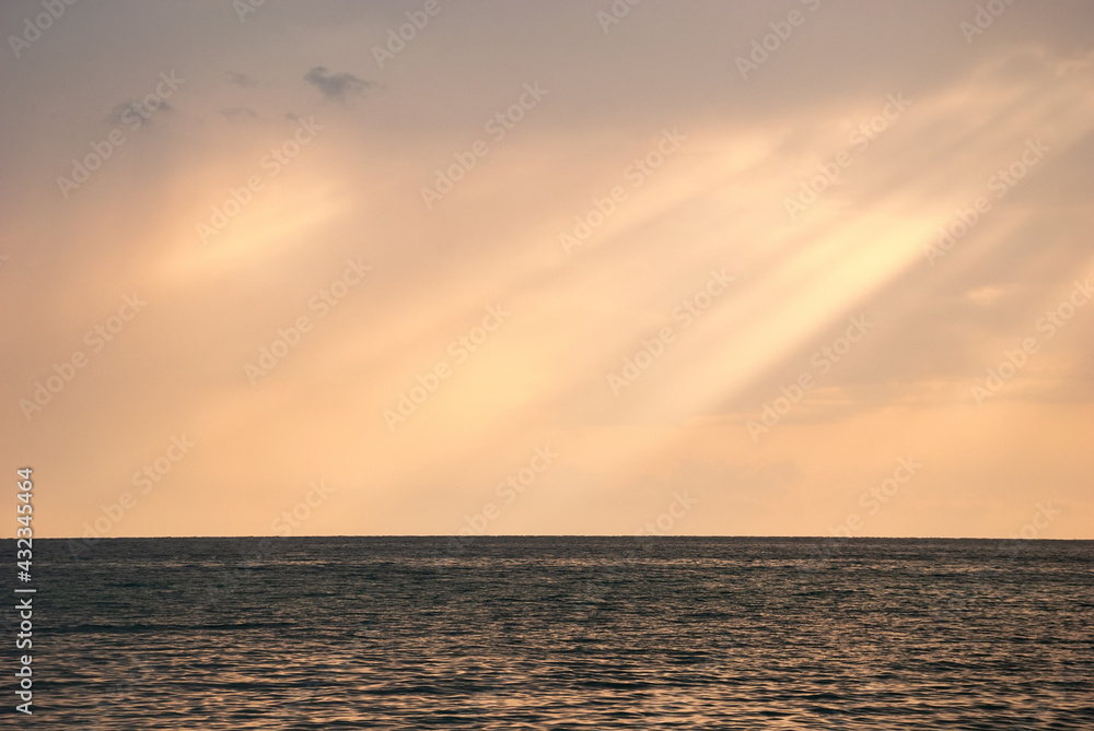 The rays of the sun break through the clouds onto the water smooth of the sea.