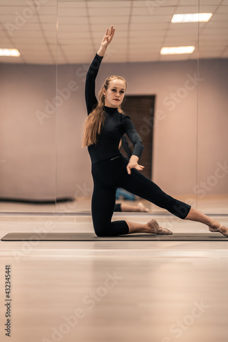 Beautiful young woman is engaged in gymnastics in the gym. The athletic body of the girl is covered with tight-fitting yoga clothes.