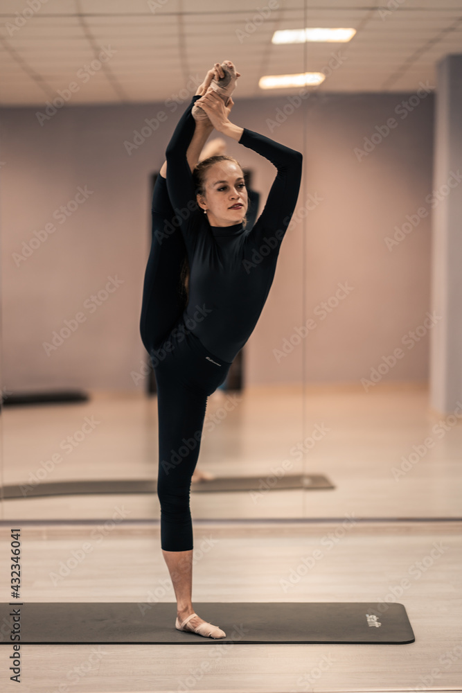 Fototapeta premium Beautiful young woman is engaged in gymnastics in the gym. The athletic body of the girl is covered with tight-fitting yoga clothes.