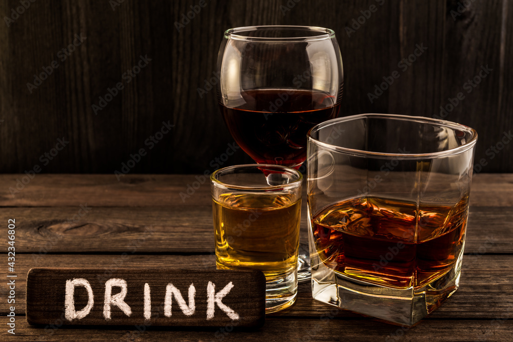 Three glasses with brandy, tequila and red wine with the wooden plank on it is an inscription Three glasses with brandy, tequila and red wine with the wooden plank on it is an inscription