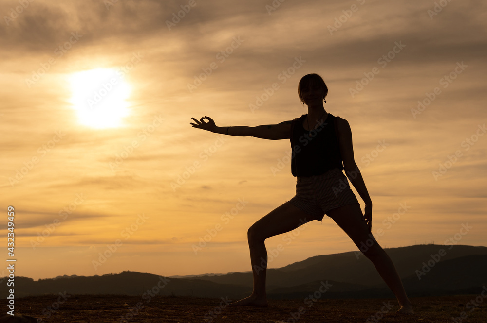 Silhouette of a  young woman practicing yoga alone on the mountains with a beautiful sunset