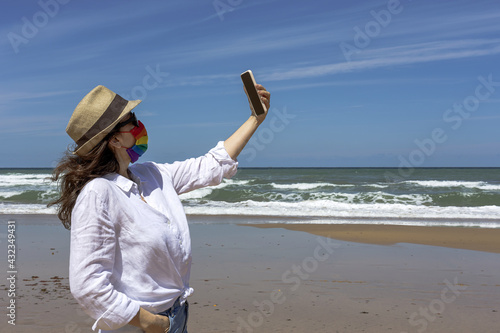 Lesbian woman on the beach with face mask with LGBT colors.
