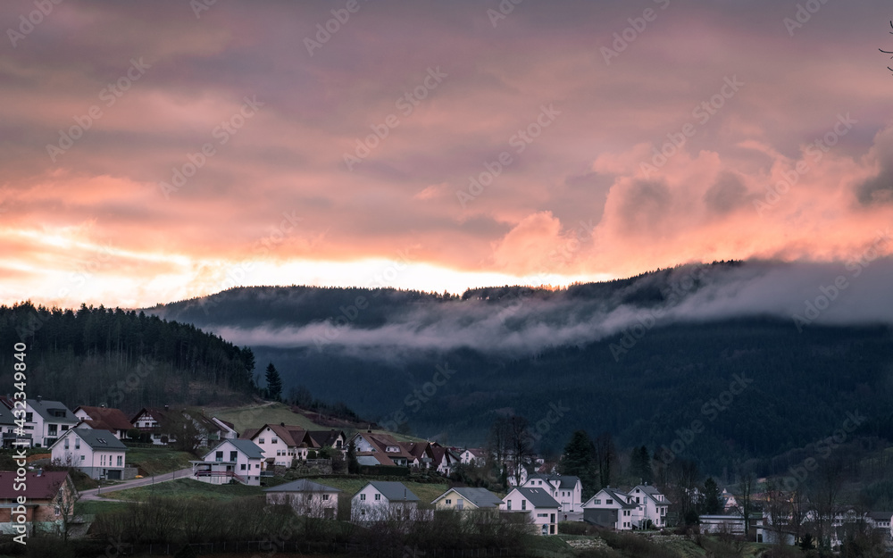 Beautiful view of the sunset in a small town in the Germany. Big mountains on the background. Fog and clouds hiding peak of the mountain. Schwarzwald nature