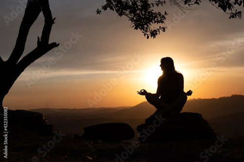 Silhouette of a young woman practicing yoga alone on the mountains with a beautiful sunset