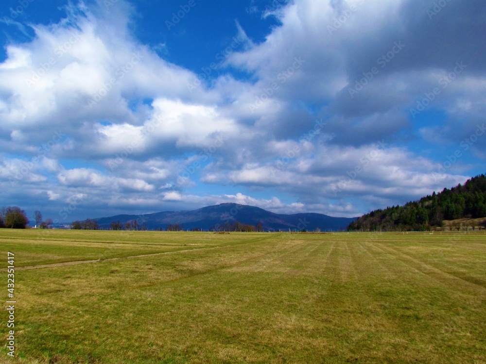 View of Slivnica hill in Notranjska, Slovenia and a field in front with white clouds in blue sky