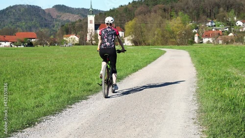 Woman cycling along sand-gravel road.