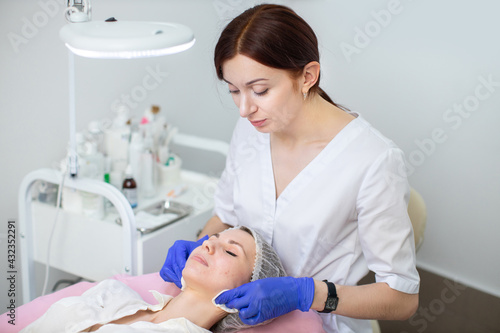 Close-up of a professional woman cosmetologist making mechanical cleaning of the face of young lady  wiping cheeks with sponges. Facial skin care at cosmetology office