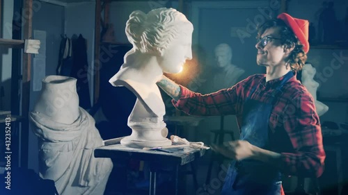 Male sculptor is looking at the gypsum bust after brushing it