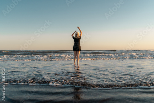 Happy woman on the shore of the beach at sunset dancing with arms in the air.