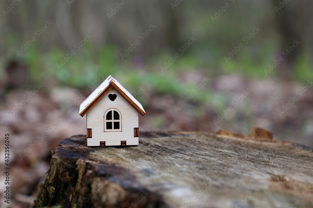 Wooden house model in a forest on mossy stump on blurred background. Concept of country cottage, real estate in ecologically clean area Wooden house model in a forest on mossy stump on blurred background. Concept of country cottage, real estate in ecologically clean area