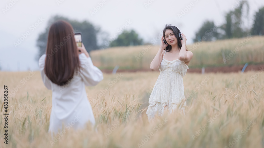 two young asian tourists girls strolling and taking pictures with smartphone in a barley demonstration plot two young asian tourists girls strolling and taking pictures with smartphone in a barley demonstration plot