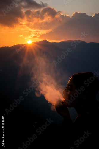 silhouette shadow Woman Holding smoke Marijuana Joint at evening and the sunlight with mountain background .