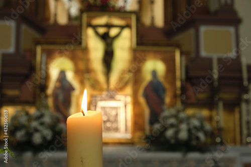 Obraz na plátně Lighted candle with a catholic altarpiece on the bottom with a crucified christ