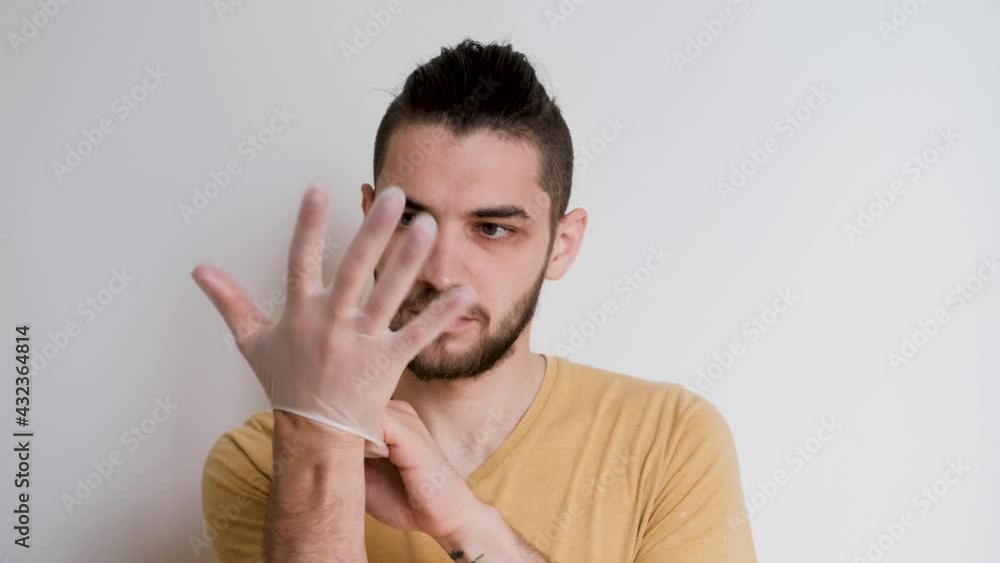 Young, cute white Caucasian man with beard puts gloves and white protective medical mask on his face. Individual protection against viruses and bacteria. Video footage 4k.