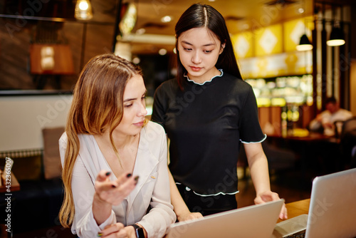 Young diverse women working with laptop in cafe