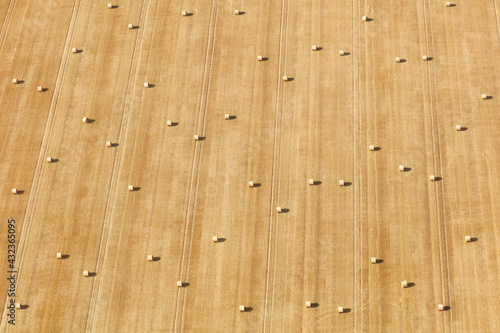 An aerial photograph taken from a helicopter of a field of wheat in the UK at the end of summer. Many hay bales can be seen in a bright yellow field making a beautiful striped background pattern.