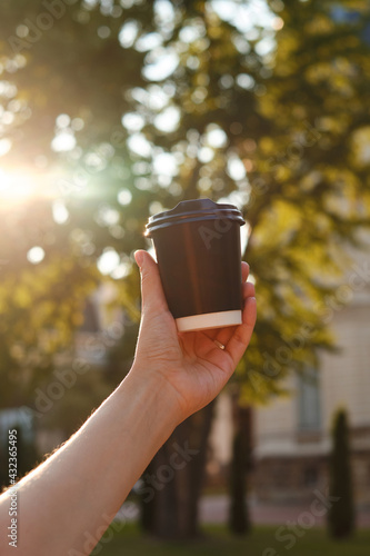 Black paper cup with coffee in woman hand. Time for drinking coffee in the city. Disposable paper cup closeup. Blank space for text, mockup. Concept of coffee to go, takeaway drinks, morning snack.
