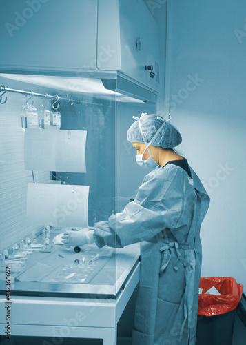 Female scientist working in the fume hood with a mask, cap, gloves and plastic pretreatment gown in the study against covid-19