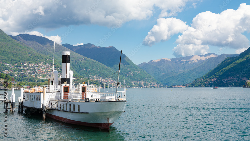 Industrial vessel on the waters of Lake Como, Como, Italy. Italian alps, with forests, blue sky and white clouds on the background.
