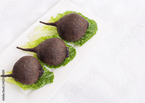 three whole organic unpeeled baked beetroots green lettuce leaves on white plate. healthy nutrition, vegetarian, vegetables diet, minimalistic lifestyle concept. copy space. isolated