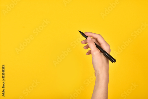 Girl's hand with a pen on a yellow background. Advertising inscription. photo