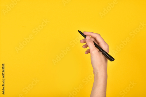 Foto Girl's hand with a pen on a yellow background