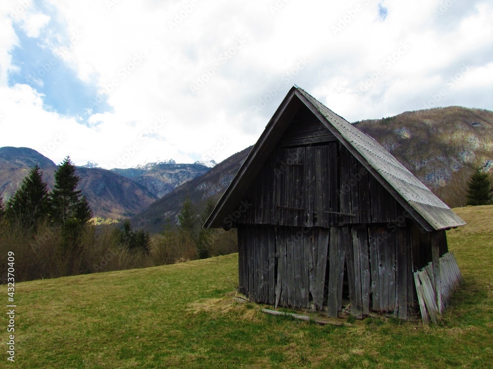 Old shabby wooden abandoned crumbling house on a meadow and forest covered mountans in Julian alps and Triglav national park in Gorenjska, Slovenia Old shabby wooden abandoned crumbling house on a meadow and forest covered mountans in Julian alps and Triglav national park in Gorenjska, Slovenia