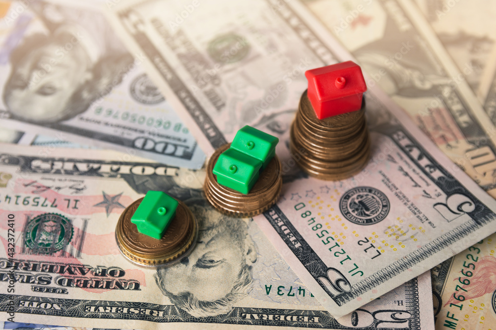 Fototapeta premium Miniature colorful red and green houses on stack coins and dollar banknotes. Finance and property investment concept. Real estate investment.