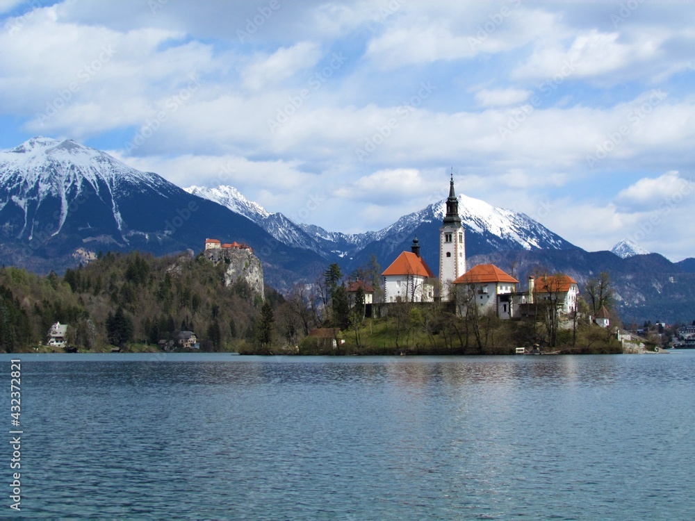 View of the church on the island on lake Bled and Bled castle and snow covered peaks of Karavanke mountains with mountain Stol behind in Gorenjska, Slovenia