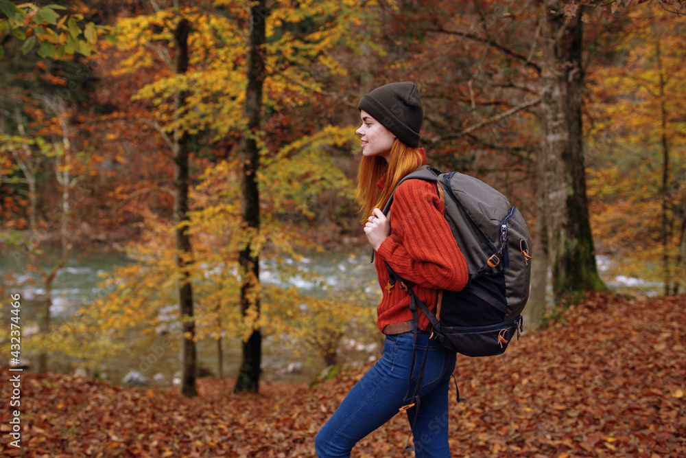 woman in autumn park with fallen leaves and backpack on her back river in the background woman in autumn park with fallen leaves and backpack on her back river in the background