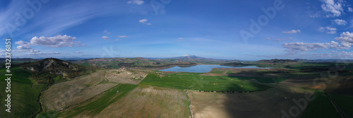 180 degree aerial photo of Ogliastro lake in the heart of Sicily with Etna view. Place of great naturalistic value surrounded by hills planted with cereals. A destination for migratory bird species.