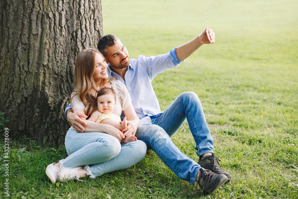 Making family memories. Happy parents mom and dad with baby girl daughter taking photo selfie with smartphone camera in park. Man, woman, baby talking on video chat call on cell phone outdoors. Making family memories. Happy parents mom and dad with baby girl daughter taking photo selfie with smartphone camera in park. Man, woman, baby talking on video chat call on cell phone outdoors.