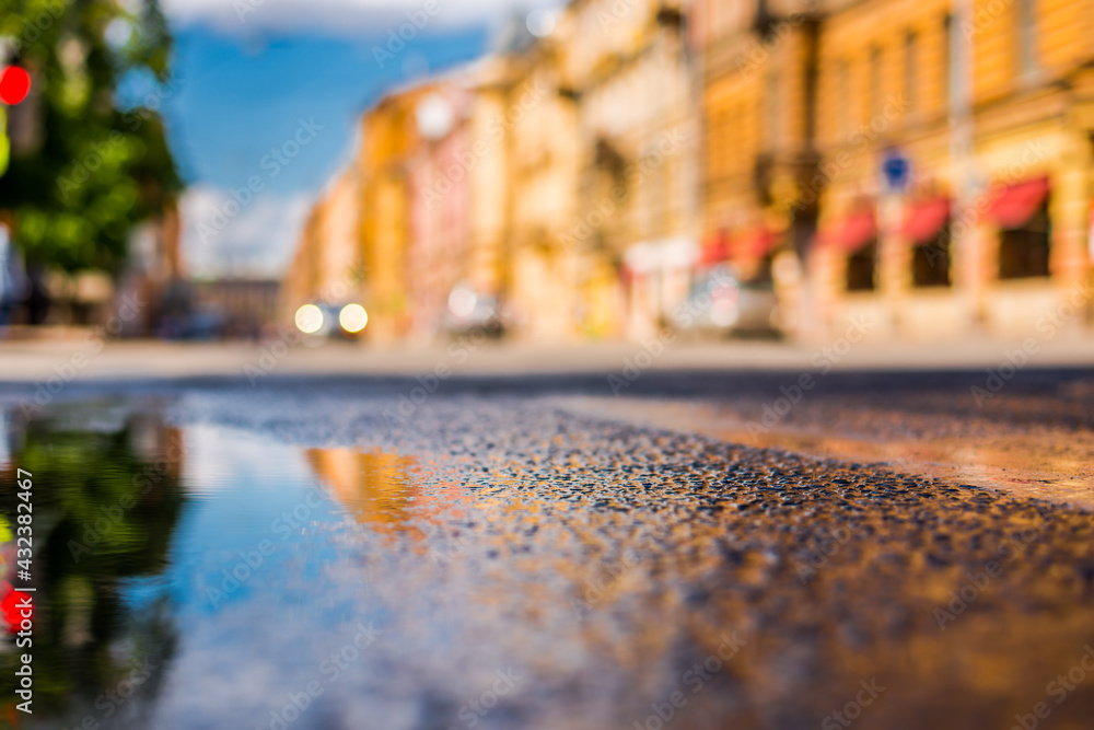 Obraz premium Sunny day after rain in the city, the headlights of the approaching car on the road. Close up view from the level of the puddle on the pavement
