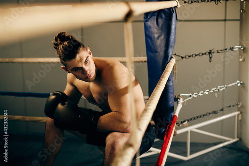 Young boxer sitting in corner of boxing ring during sports training in a gym.