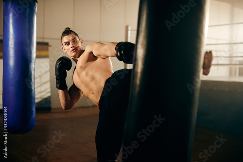 Male fighter kicking punching bag while working out at boxing club. © Drazen