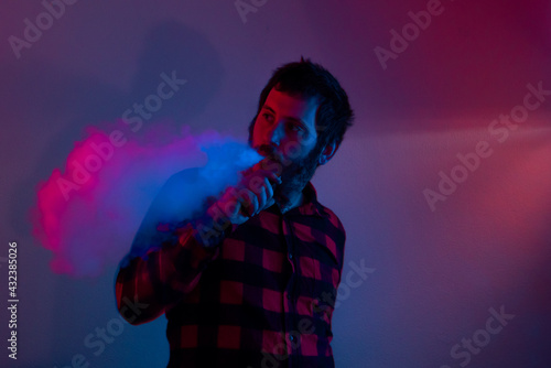 man vaping and throwing smoke with colors on crumpled background. person using electronic cigarette illuminated with pink and blue lights,