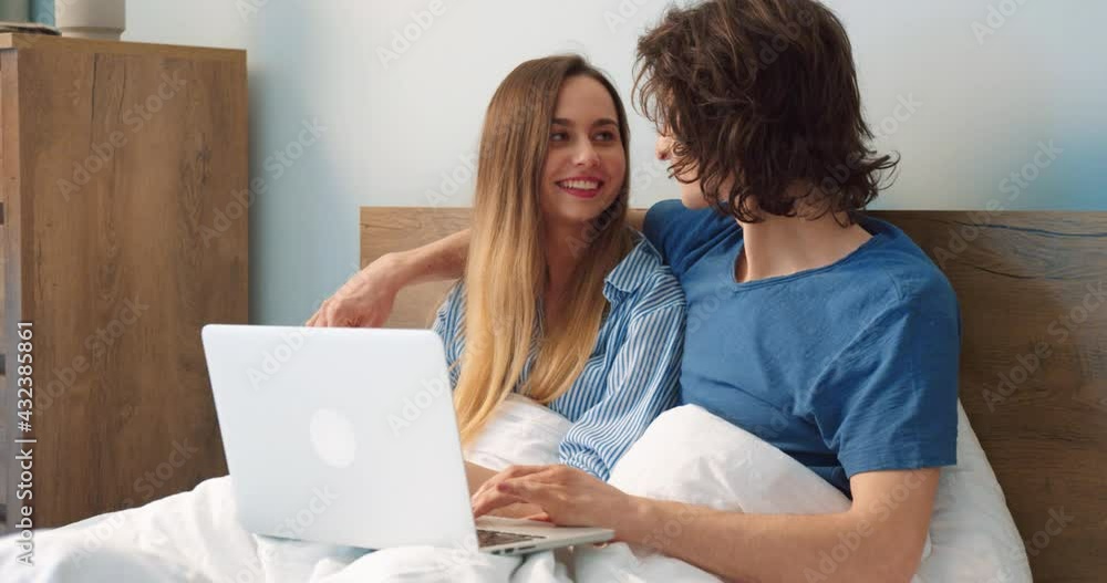 Waist up portrait of the woman sitting with her husband and watching something funny at the laptop while spending weekend at home at the weekend. Couple laughing while watching movie Waist up portrait of the woman sitting with her husband and watching something funny at the laptop while spending weekend at home at the weekend. Couple laughing while watching movie