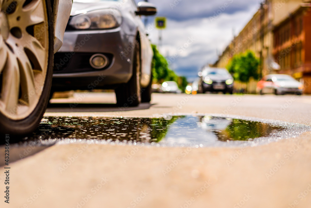 Sunny day after rain in the city, the headlights of the approaching car. Close up view of a wheel of a car parked in a puddle level Sunny day after rain in the city, the headlights of the approaching car. Close up view of a wheel of a car parked in a puddle level