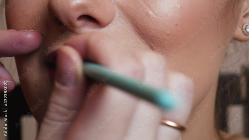 The makeup artist applies red lipstick on the female lip The makeup artist applies red lipstick on the female lip