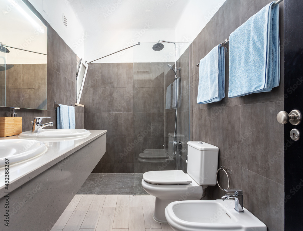 Modern tiled gray bathroom of a resort, with a sink facing a toilet and