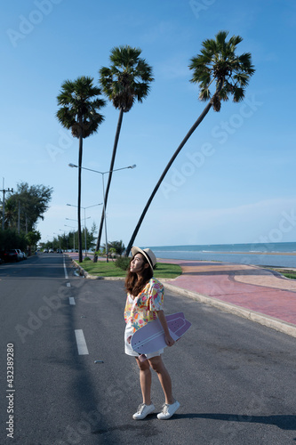 Asian woman hold surfskate or skate board in front of Three coconut palm trees on blue sky background at Pranburi, Prachuabkirikhan province, Thailand. photo