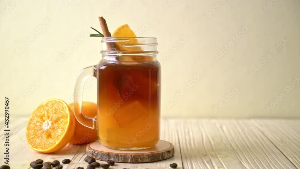 A glass of iced americano black coffee and layer of orange and lemon juice decorated with rosemary and cinnamon A glass of iced americano black coffee and layer of orange and lemon juice decorated with rosemary and cinnamon