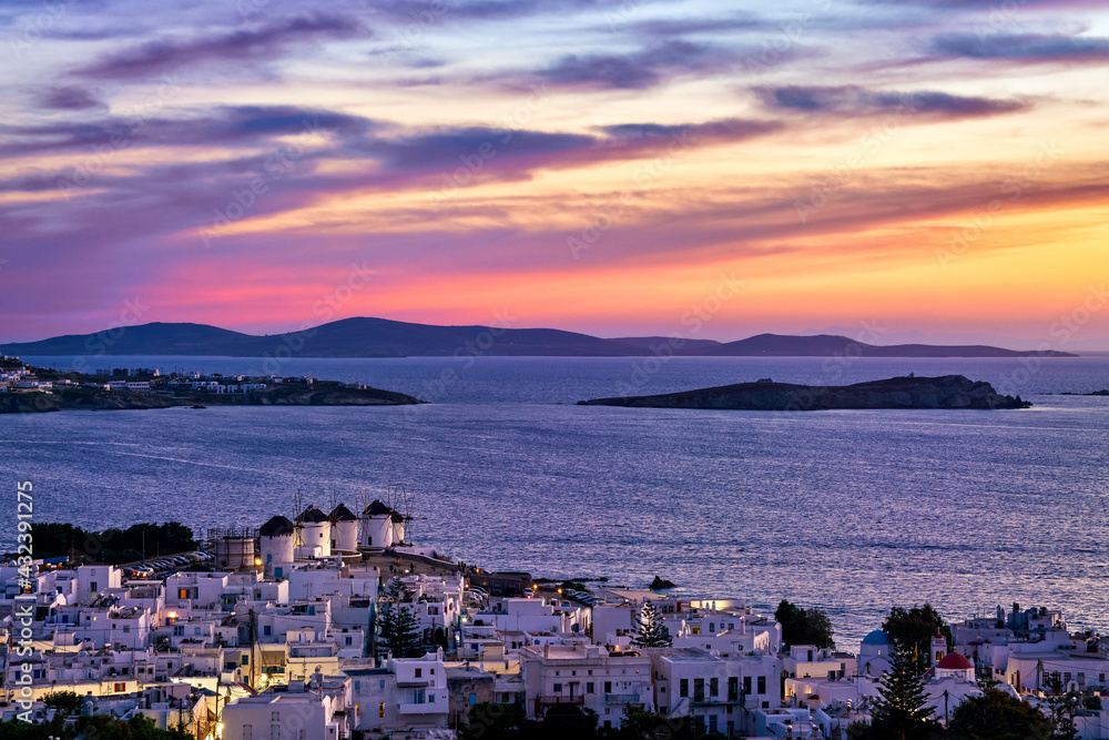 Colorful sunset view famous traditional white windmills, Mykonos, Greece. Whitewashed houses, colorful sunset sky, summer destination, town lights on