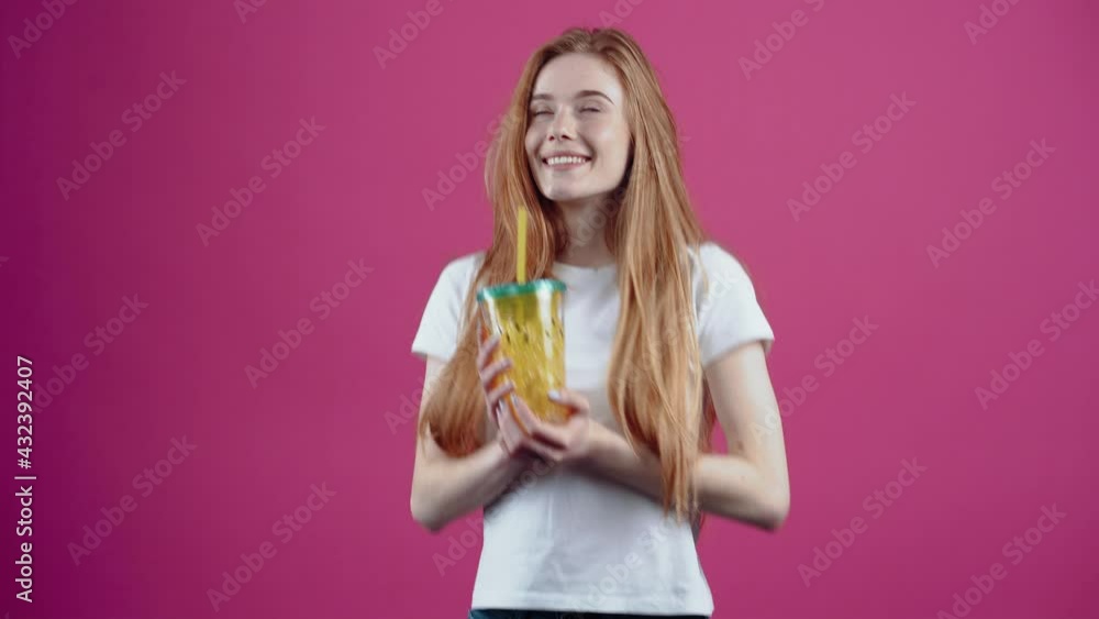The red-haired student, satisfied with a glass of juice in her hand, smiles dreamily. Freckled teenage girl in a white T-shirt, isolated on a pink background. The concept of people's lifestyle The red-haired student, satisfied with a glass of juice in her hand, smiles dreamily. Freckled teenage girl in a white T-shirt, isolated on a pink background. The concept of people's lifestyle