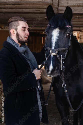 A man in a black coat holds a black horse