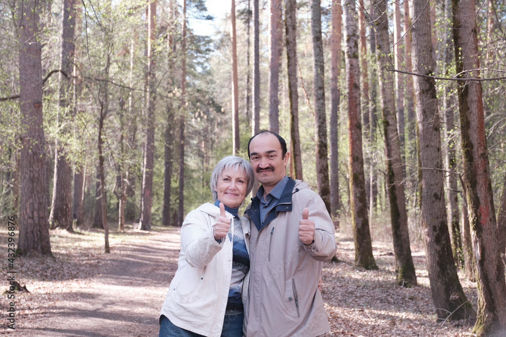 Elderly interracial couple in a spring forest park showing a thumbs up gesture that means We like it Elderly interracial couple in a spring forest park showing a thumbs up gesture that means We like it