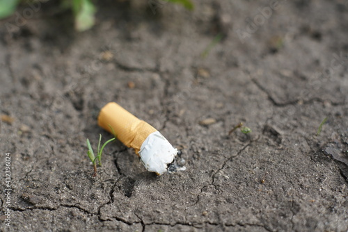 The cigarette butt is lying on the black ground with cracks. Closeup. Space for text