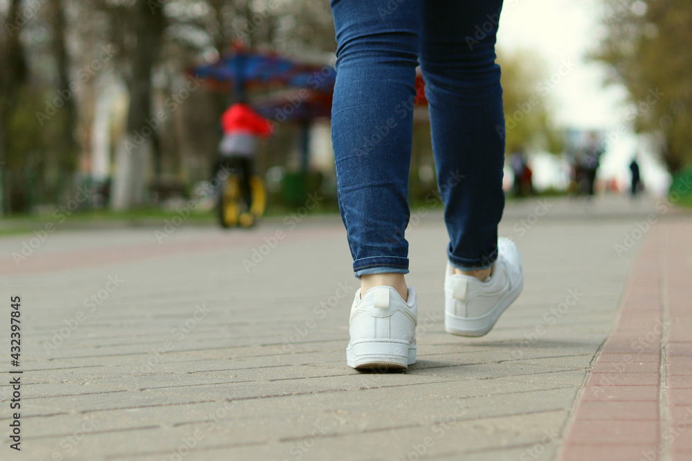 Women's legs in jeans and white sneakers walk in the park Women's legs in jeans and white sneakers walk in the park