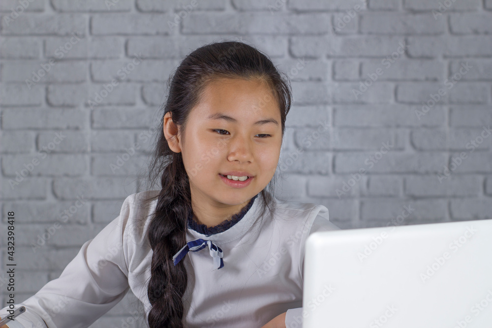 Little laughing asian girl studying at home in online class learning online video call. She attends online school lessons with a laptop and takes notes at home. New normal. Stay indoors. Little laughing asian girl studying at home in online class learning online video call. She attends online school lessons with a laptop and takes notes at home. New normal. Stay indoors.